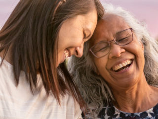 Mother with white hair and daughter with brown hair lovingly touching heads, laughing