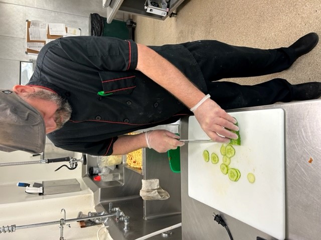 Matt, Cook at Redeemer Health Care Center, slices cucumber grown in the garden. 