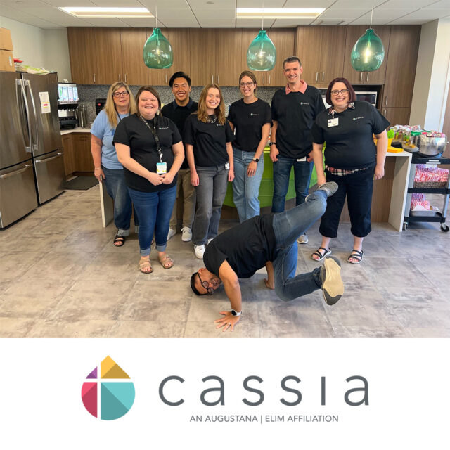 Members of the Cassia committee pose for a group photo in a kitchen area during a State Fair-inspired picnic, with one member playfully striking a breakdance pose in front.