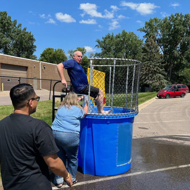 A Cassia employee reacts as ice is being added to the dunk tank water while they sit on the edge, surrounded by colleagues during a State Fair-inspired picnic event.
