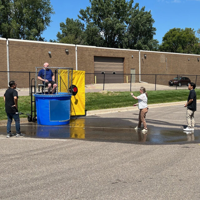 A Cassia employee takes aim at the target during a dunk tank event while colleagues watch, as another employee sits ready to be dunked during a State Fair-inspired picnic.