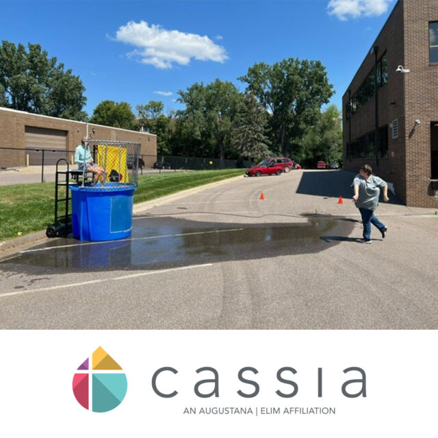 A Cassia employee runs towards a dunk tank, preparing to hit the target as another employee sits ready to be dunked during a State Fair-inspired picnic event
