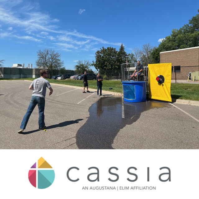 Cassia employee throws a ball at a target during a State Fair-inspired picnic, aiming to dunk a colleague sitting in a dunk tank on a sunny day.