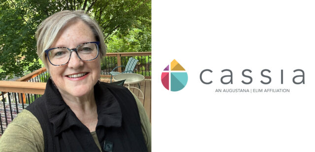 Rev. Julie Ryan, newly appointed Co-VP of Spiritual Life at Cassia, smiles while standing on an outdoor deck. She brings extensive ministry experience, having served ELCA congregations and worked as a Chaplain, to her new role at Cassia's Home Office.
