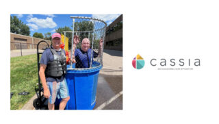 Cassia President and CEO Bob Dahl stands smiling next to a dunk tank, wearing a life jacket, while another Cassia employee sits inside the dunk tank during a sunny State Fair-inspired picnic event.