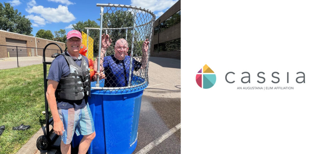 Cassia President and CEO Bob Dahl stands smiling next to a dunk tank, wearing a life jacket, while another Cassia employee sits inside the dunk tank during a sunny State Fair-inspired picnic event.