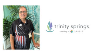 Rev. Chuck Tabor, Chaplain at Trinity Springs, stands smiling in a patriotic shirt, ready to share his compassionate spiritual care and support with the community.