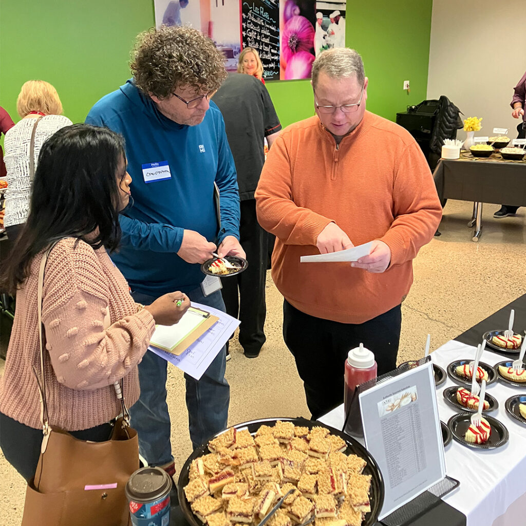 Culinary team members engage in a conversation with a vendor while sampling dessert options at the Cassia food show, focused on improving meal quality for residents.