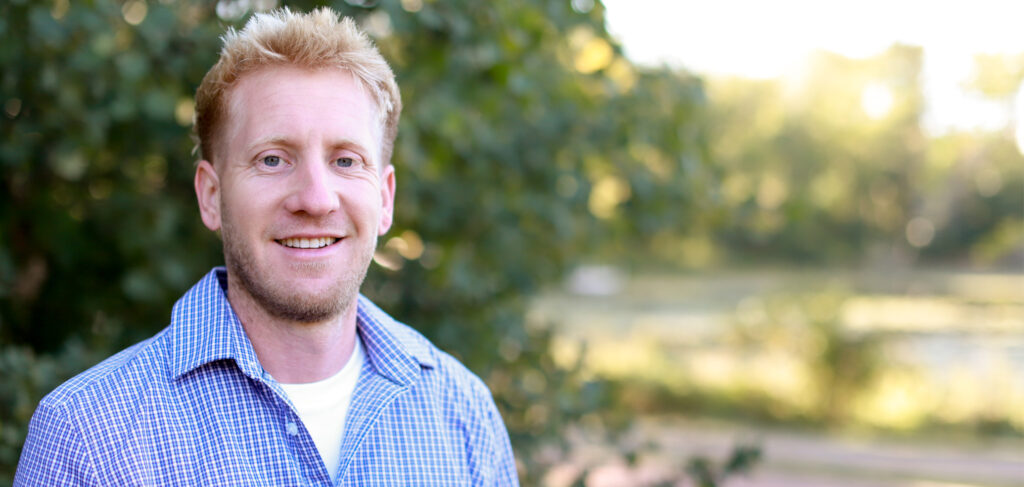 Matt, the environmental services and maintenance director at Elim Shores Assisted Living, smiling outdoors with a scenic background of trees and water.
