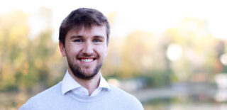 Sam Pahl smiling outdoors with a blurred natural background.