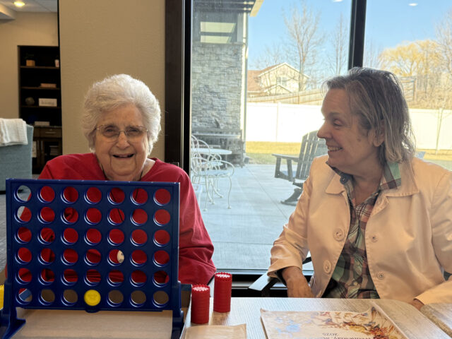 Two Meadowview of Davenport memory care residents enjoy a game of Connect Four together, smiling and sharing a joyful moment indoors.