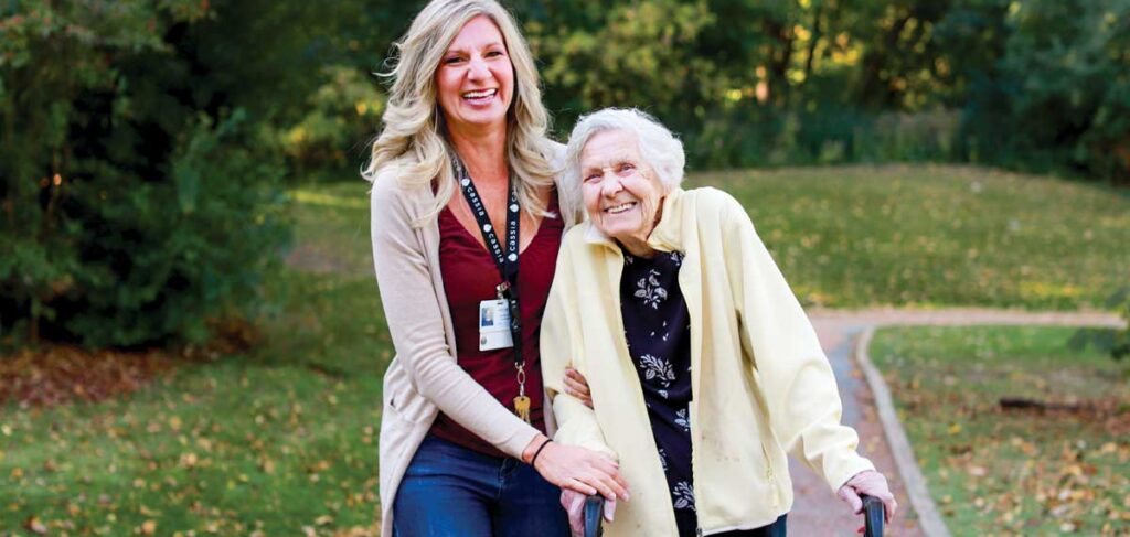 Elim Shores resident walking with a caregiver on the lakeside path, enjoying fullness of life and scenic nature.