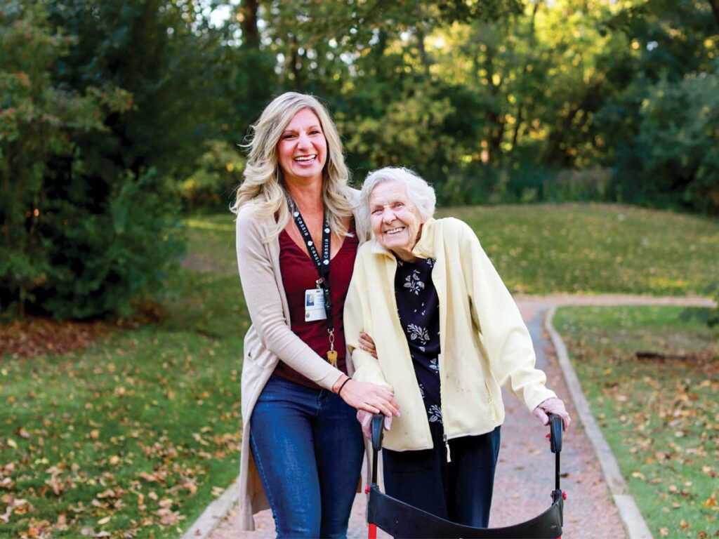 Elim Shores resident walking with a caregiver on the lakeside path, enjoying fullness of life and scenic nature.