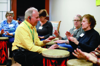 Staff member and Open Circle Adult Day Services participants engaging in hands-on drumming session.