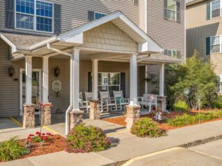 Exterior view of Newton Village Assisted Living entrance with rocking chairs, flowers, and welcoming front porch.