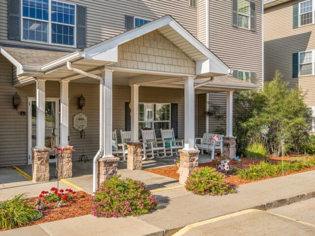 Exterior view of Newton Village Assisted Living entrance with rocking chairs, flowers, and welcoming front porch.