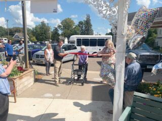 Resident cuts a ribbon during the celebration of a new donor-funded bus at Lake Ridge and Park View Assisted Living, surrounded by community members and balloons.