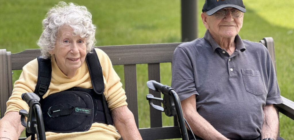 Jean, a Meadowview of Davenport memory care resident, sitting outdoors on a bench with another resident enjoying time together in the courtyard.