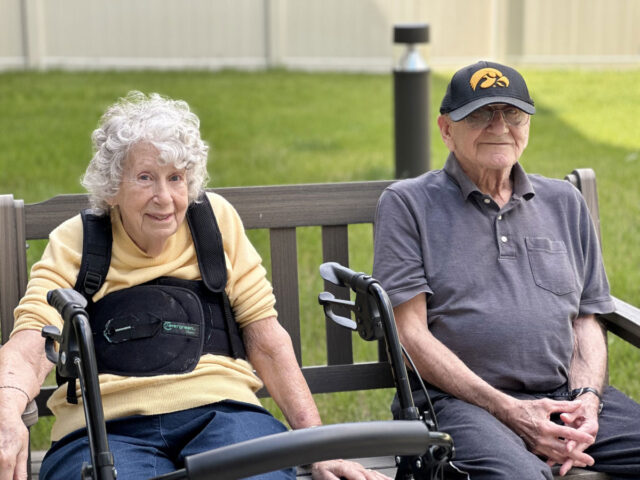 Jean, a Meadowview of Davenport memory care resident, sitting outdoors on a bench with another resident enjoying time together in the courtyard.