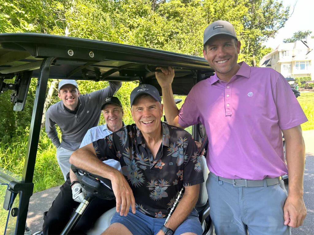 Four golfers smiling together next to a golf cart during the 2025 Cassia Golf Tournament.