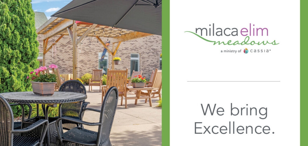 Outdoor patio seating at Milaca Elim Meadows with tables, chairs, pergola and landscaping alongside branding that reads “We bring Excellence.”