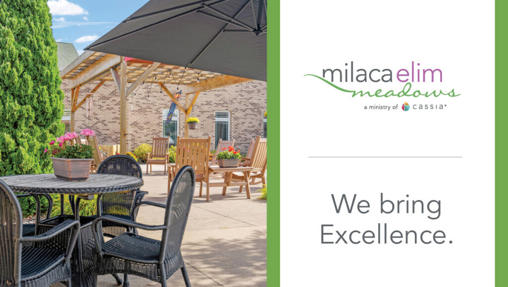 Outdoor patio seating at Milaca Elim Meadows with tables, chairs, pergola and landscaping alongside branding that reads “We bring Excellence.”