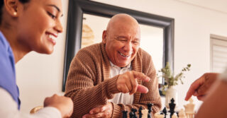 Senior enjoying a chess game with a caregiver, highlighting connection and independence in a familiar community setting.