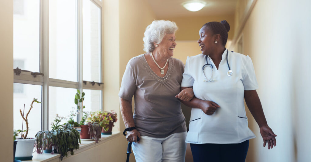 Senior resident walking with caregiver in assisted living community hallway