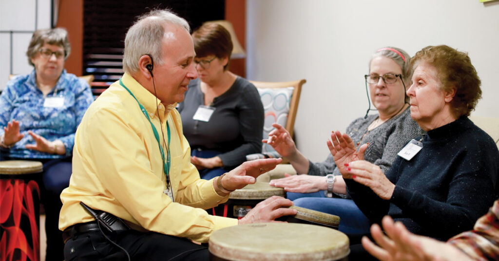 Adults participating in a dementia arts program play hand drums together during a music session at Open Circle, supporting connection, expression, and engagement