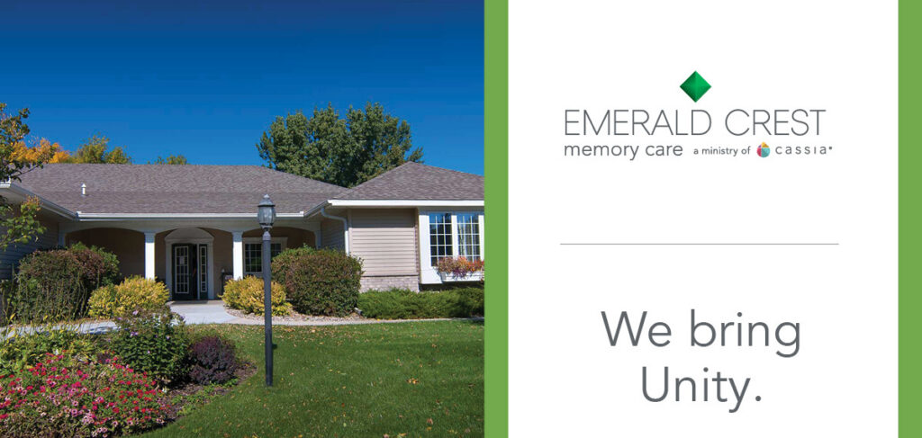 Exterior view of Emerald Crest memory care community with landscaped lawn and flowers, alongside branding text reading “Emerald Crest Memory Care” and the message “We bring Unity.”