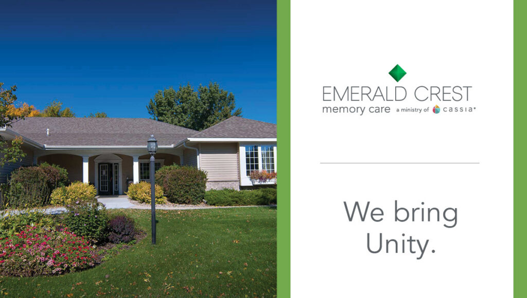 Exterior view of Emerald Crest memory care community with landscaped lawn and flowers, alongside branding text reading “Emerald Crest Memory Care” and the message “We bring Unity.”