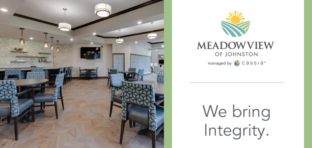Interior common area at Meadowview of Johnston featuring dining tables, upholstered chairs, a bar seating area, and a television in a bright, modern senior living community. Branding on the image reads “Meadowview of Johnston” and “We bring Integrity.”