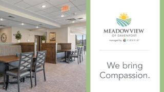 Meadowview of Davenport’s dining room features comfortable seating, wood accents, and large windows, alongside the community logo and the message, “We bring Compassion.”