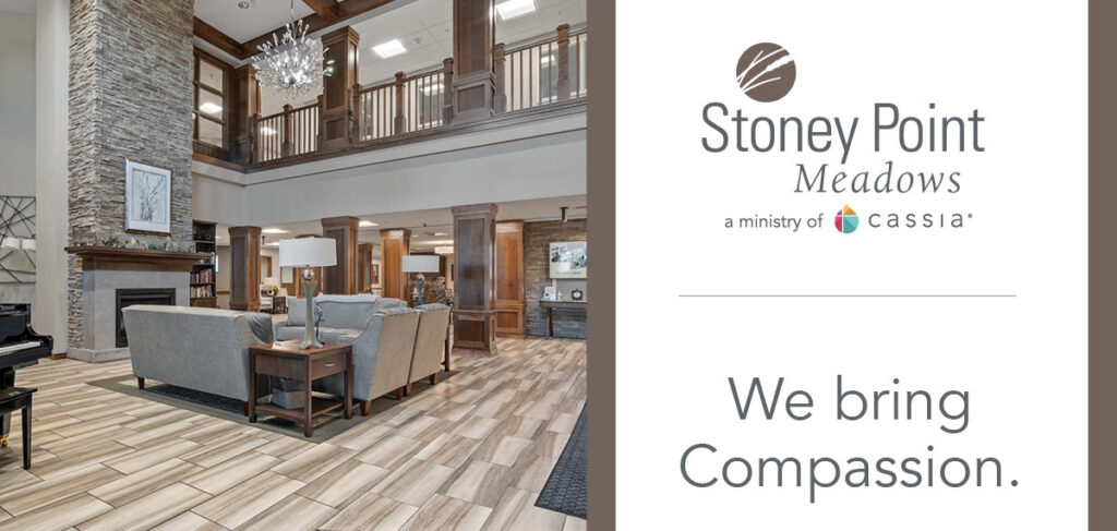Stoney Point Meadows senior living community lobby with a stone fireplace, wood accents, comfortable seating, and the message: “We bring Compassion.”