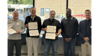 Group of five individuals posing indoors, with three holding award certificates during a recognition event.